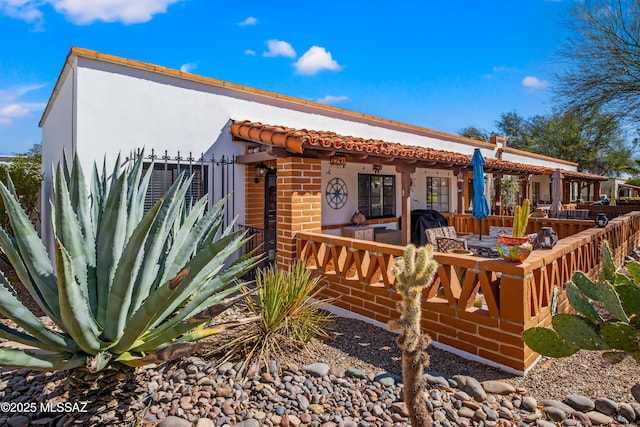 exterior space featuring stucco siding, a tile roof, an outdoor living space, and brick siding