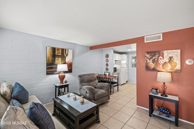 living area with an accent wall, visible vents, brick wall, and light tile patterned floors