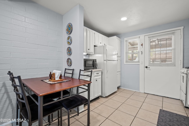 kitchen featuring light tile patterned floors, brick wall, white appliances, and white cabinetry