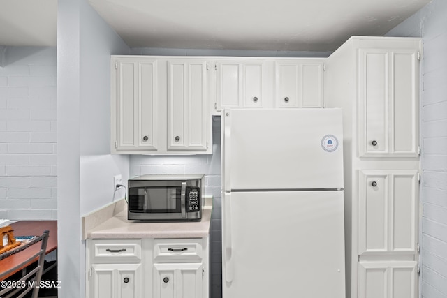 kitchen with light countertops, stainless steel microwave, freestanding refrigerator, and white cabinets