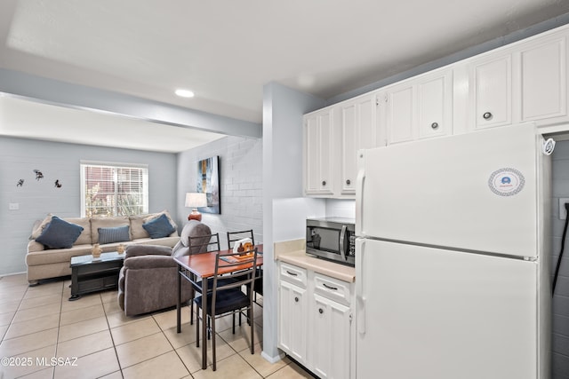 kitchen with stainless steel microwave, freestanding refrigerator, open floor plan, white cabinets, and light tile patterned flooring