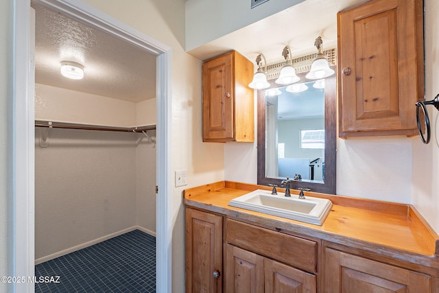 bathroom featuring a walk in closet, vanity, baseboards, and a textured ceiling