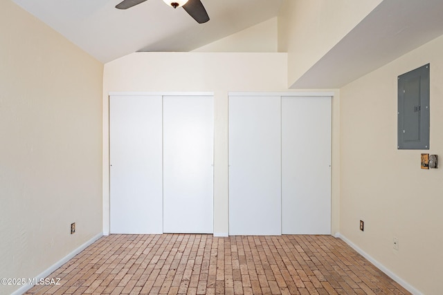 unfurnished bedroom featuring electric panel, brick floor, ceiling fan, vaulted ceiling, and multiple closets