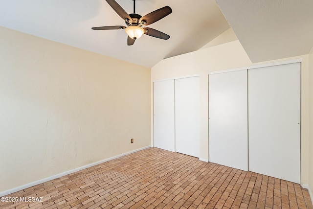 unfurnished bedroom with brick floor, lofted ceiling, two closets, and a ceiling fan