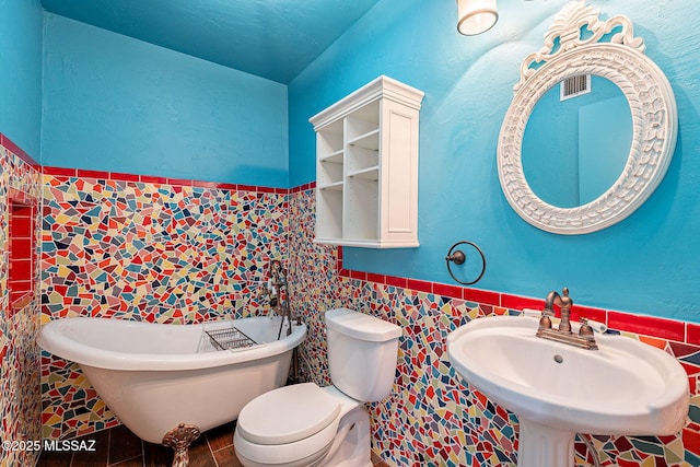 full bath with a wainscoted wall, a freestanding bath, a sink, tile walls, and toilet