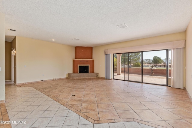 unfurnished living room featuring visible vents, a fireplace with raised hearth, a textured ceiling, light tile patterned flooring, and baseboards