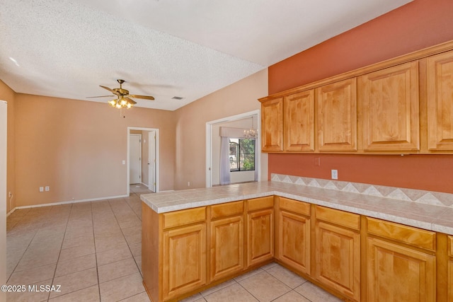 kitchen with a ceiling fan, a textured ceiling, tile countertops, a peninsula, and light tile patterned floors