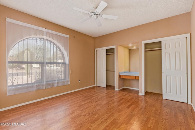 unfurnished bedroom featuring multiple windows, a textured ceiling, two closets, and wood finished floors