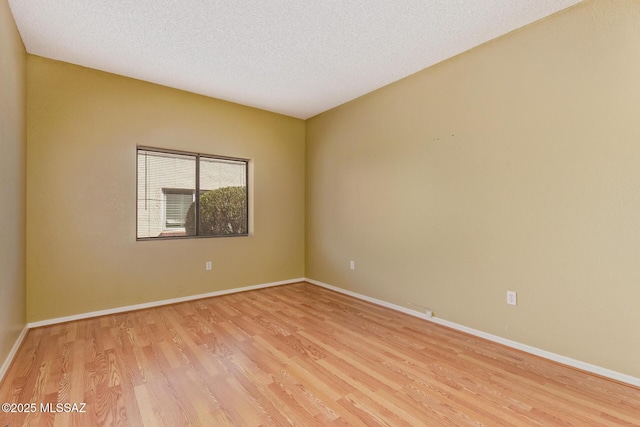 spare room with light wood-style flooring, baseboards, and a textured ceiling