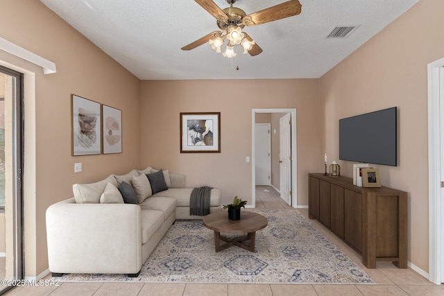 living area with visible vents, a textured ceiling, light tile patterned floors, baseboards, and ceiling fan