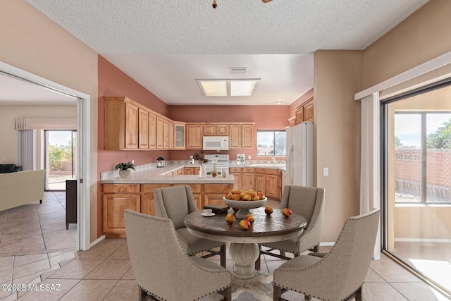 kitchen featuring glass insert cabinets, light countertops, light tile patterned flooring, white appliances, and a sink