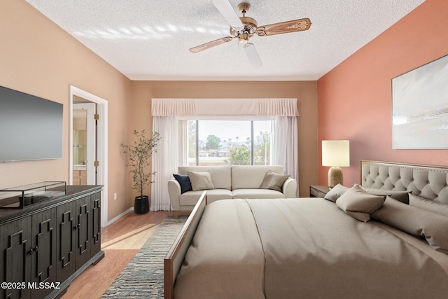 bedroom with connected bathroom, baseboards, light wood-type flooring, a textured ceiling, and a ceiling fan