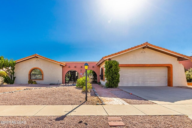 mediterranean / spanish house with stucco siding, an attached garage, driveway, and a tiled roof