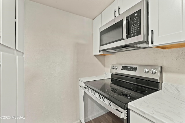 kitchen featuring a textured wall, stainless steel appliances, wood finished floors, and white cabinets