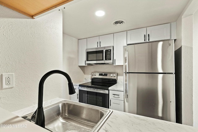 kitchen featuring a textured wall, a sink, visible vents, white cabinets, and appliances with stainless steel finishes