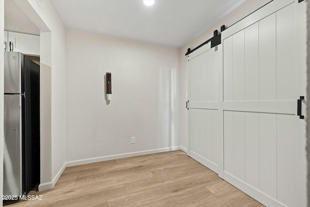 unfurnished room featuring baseboards, a barn door, and light wood-style floors