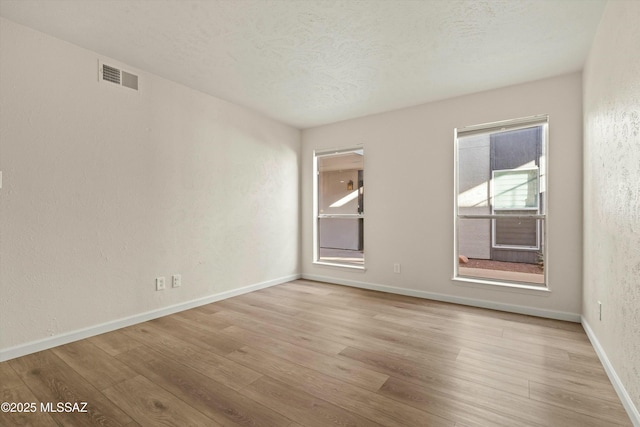 empty room with visible vents, a textured ceiling, light wood-style flooring, and baseboards