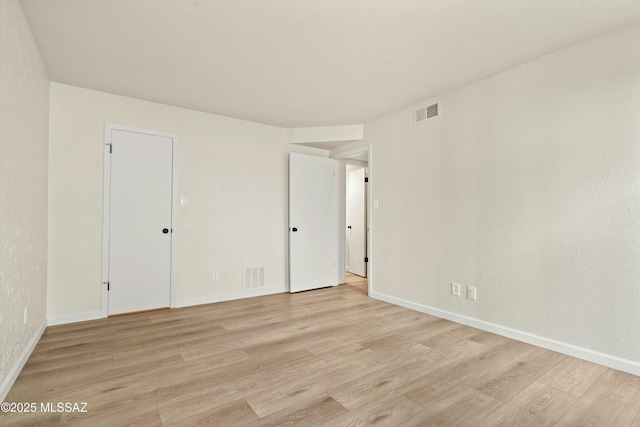 empty room featuring light wood-type flooring, visible vents, and baseboards