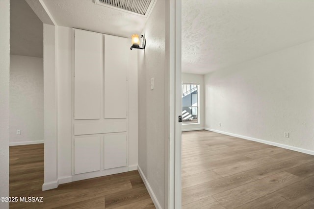 corridor featuring a textured ceiling, wood finished floors, visible vents, and baseboards