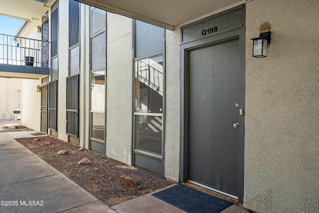 view of exterior entry featuring a balcony and stucco siding