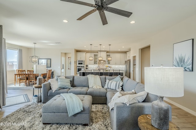 living area with ceiling fan with notable chandelier, recessed lighting, light wood-style floors, and baseboards