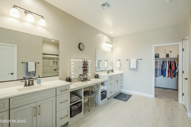 full bath featuring visible vents, tiled shower, two vanities, a sink, and a walk in closet