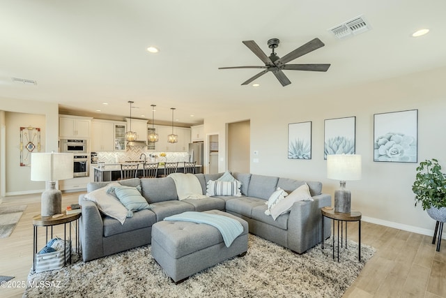 living room featuring light wood finished floors, visible vents, baseboards, ceiling fan, and recessed lighting