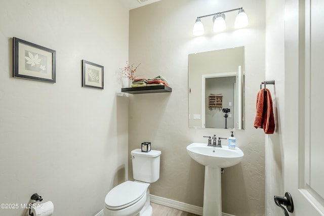 half bathroom with a sink, baseboards, and toilet