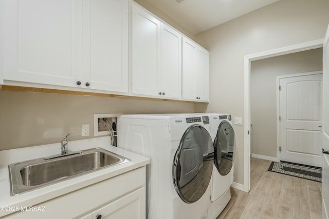 laundry area featuring light wood finished floors, baseboards, cabinet space, independent washer and dryer, and a sink