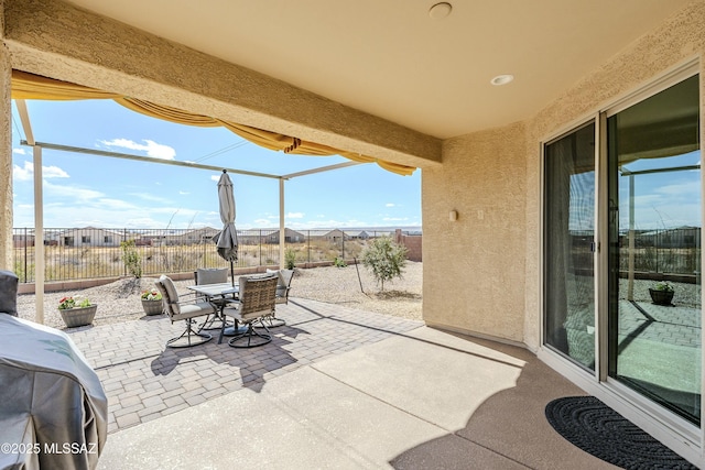 view of patio / terrace with glass enclosure, outdoor dining space, and fence