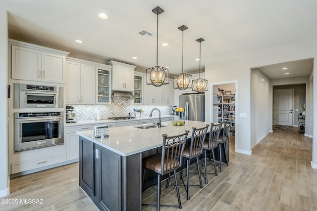 kitchen featuring visible vents, light wood finished floors, a sink, decorative backsplash, and appliances with stainless steel finishes