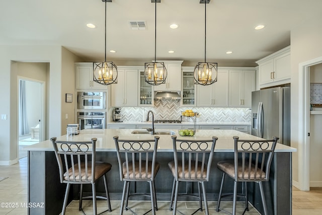 kitchen featuring visible vents, under cabinet range hood, a notable chandelier, white cabinets, and stainless steel appliances