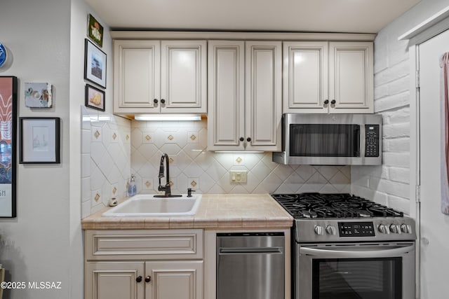 kitchen featuring appliances with stainless steel finishes, cream cabinetry, a sink, and tasteful backsplash