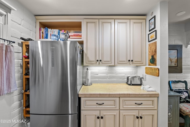 kitchen with light countertops, cream cabinetry, freestanding refrigerator, and decorative backsplash