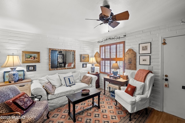 living area with ceiling fan, brick wall, and wood finished floors