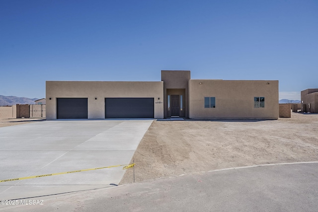 pueblo-style house with a garage, concrete driveway, fence, and stucco siding