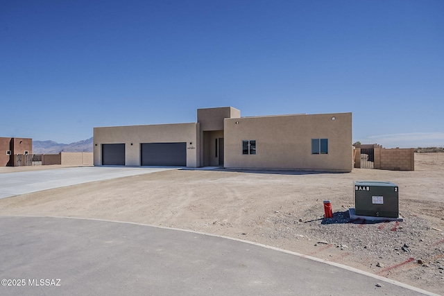 pueblo revival-style home with driveway, an attached garage, fence, and stucco siding