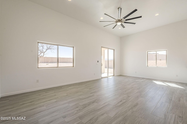 spare room featuring light wood-style flooring, a high ceiling, baseboards, and recessed lighting