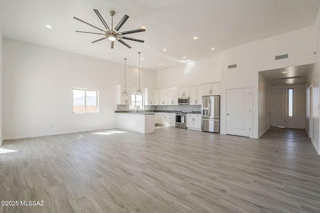 unfurnished living room with a towering ceiling, light wood-type flooring, visible vents, and a sink