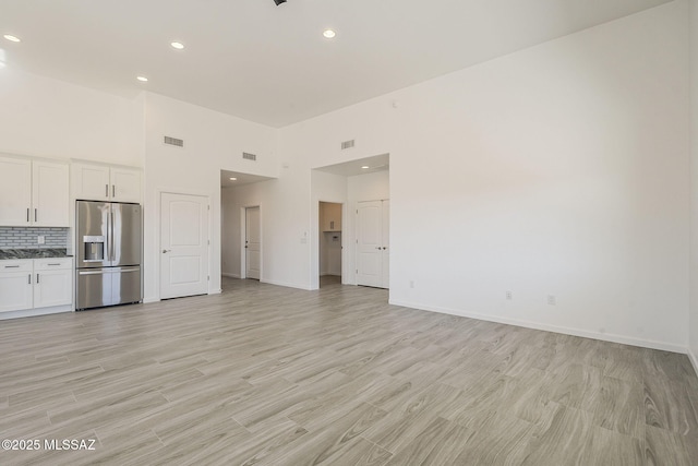 unfurnished living room with baseboards, visible vents, light wood-style flooring, and a towering ceiling