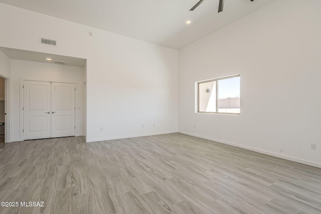 empty room with ceiling fan, a towering ceiling, baseboards, visible vents, and light wood-style floors