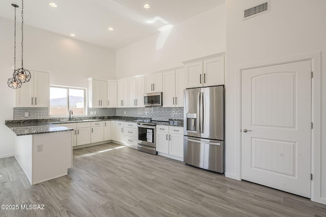 kitchen with a towering ceiling, a peninsula, stainless steel appliances, white cabinetry, and a sink