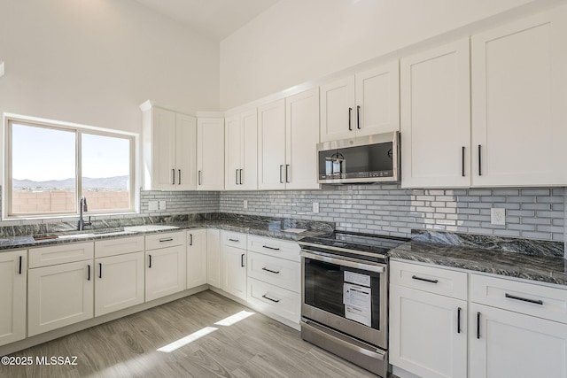 kitchen with stainless steel appliances, dark stone counters, light wood-style flooring, and decorative backsplash