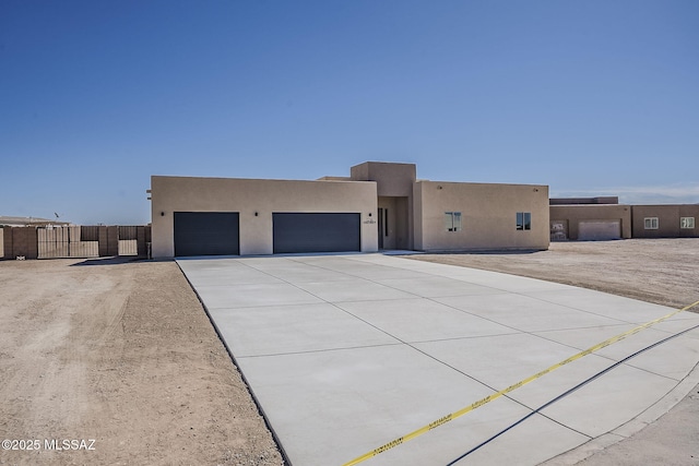 adobe home with a garage, concrete driveway, a gate, fence, and stucco siding