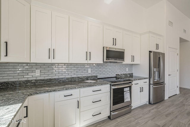 kitchen featuring tasteful backsplash, appliances with stainless steel finishes, dark stone countertops, and white cabinets