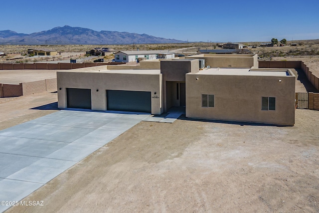 pueblo revival-style home with driveway, fence, a mountain view, and stucco siding