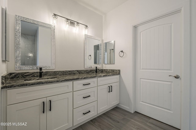 full bath featuring double vanity, a tile shower, a sink, and wood finished floors