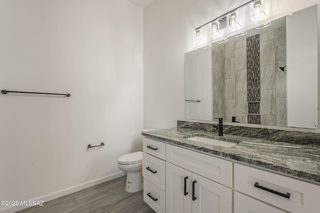 full bath with toilet, tiled shower, vanity, and baseboards