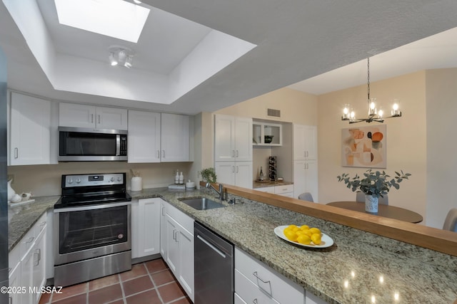 kitchen featuring appliances with stainless steel finishes, a raised ceiling, white cabinets, and a sink