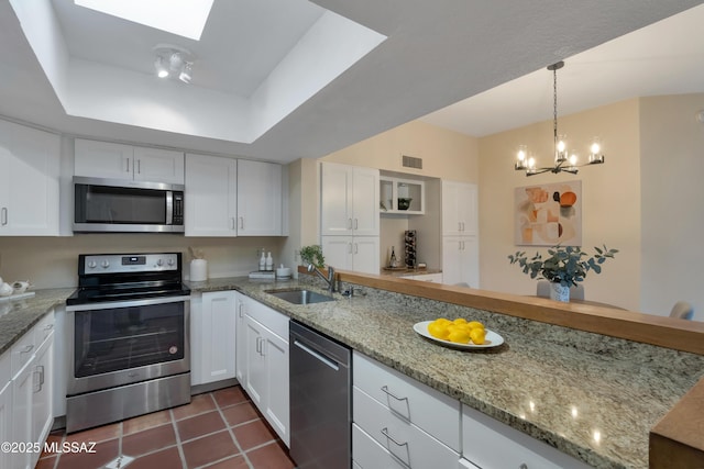 kitchen with stainless steel appliances, a tray ceiling, a sink, and white cabinetry